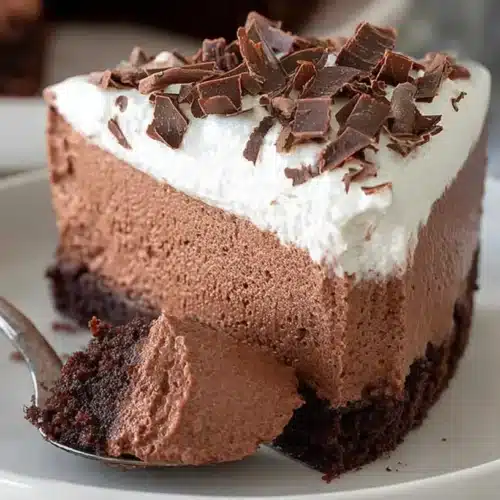 A slice of gluten-free chocolate mousse cake with brownie base, creamy mousse filling, and whipped cream topping on a white plate.