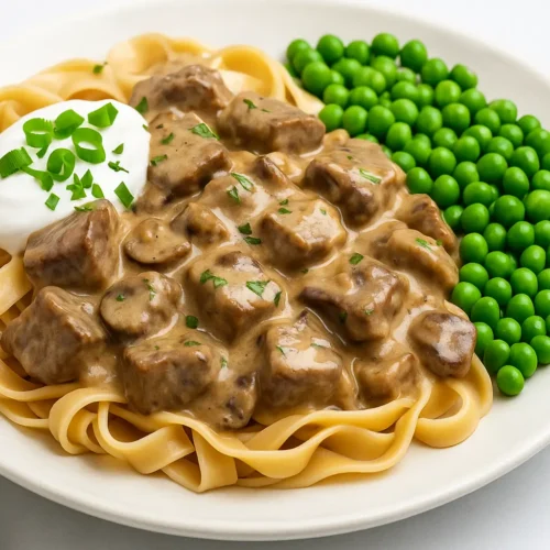 Gluten-Free Beef Stroganoff with creamy mushroom sauce, noodles, and green peas on a white plate