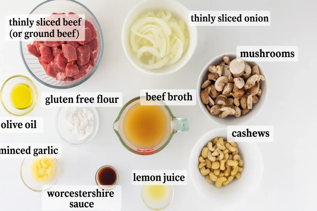 Ingredients for gluten-free beef stroganoff including beef, mushrooms, onions, garlic, cashews, broth, and sauces, neatly labeled on a white background
