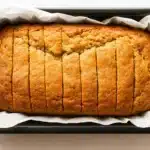 A freshly baked gluten egg free banana bread in a parchment-lined pan, golden and sliced, ideal for allergy-friendly baking.