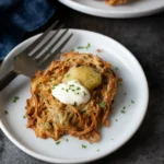 Gluten free potato latkes topped with sour cream and applesauce on a white plate