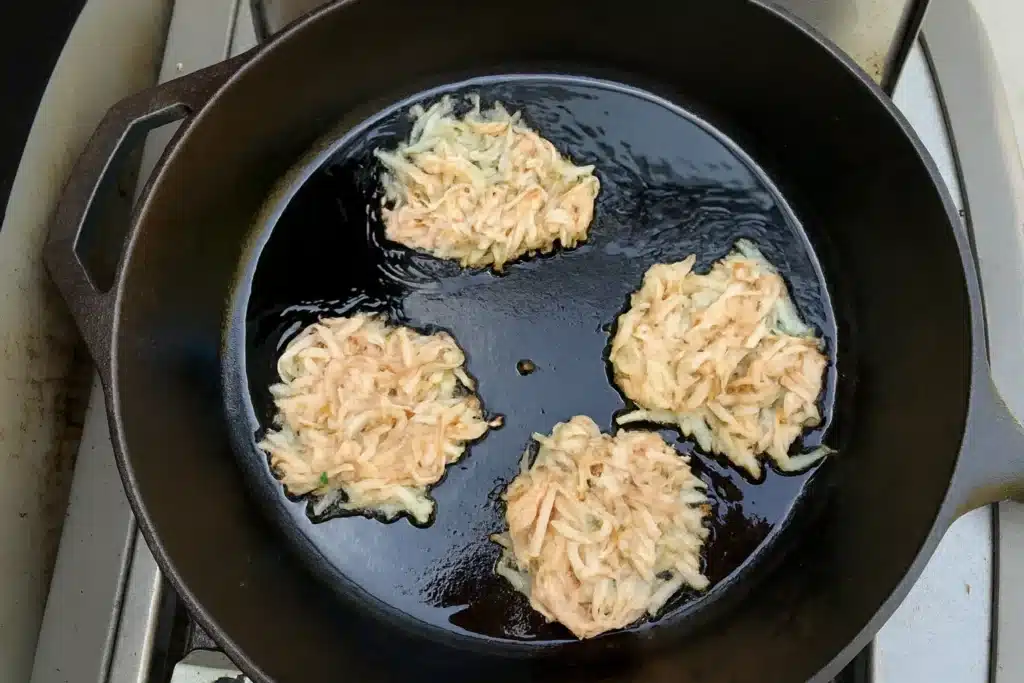 Gluten free potato latkes frying in cast iron skillet for perfect crisp texture
